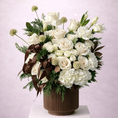White rose arrangement in a brown ribbed vase with dark ribbon accents