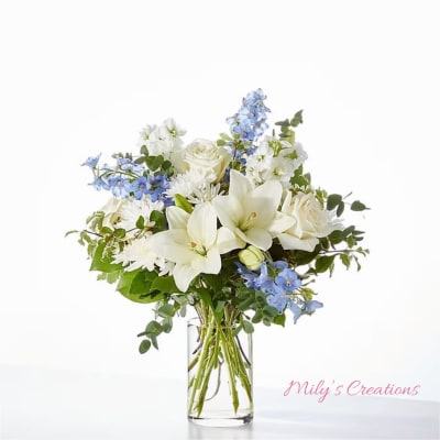 White lilies, roses, and blue delphinium arranged in a clear glass cylinder vase