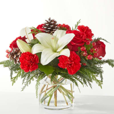 Red roses and carnations with a white lily in a glass vase
