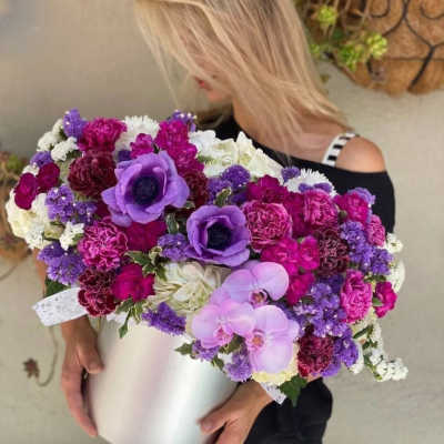 Woman holding a large purple, pink, and white flower arrangement in a white box