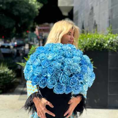 Woman holding a large bouquet of bright blue roses in a black vase