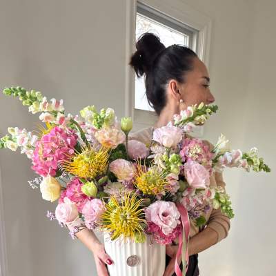 Woman holding a large pastel flower arrangement in a white vase