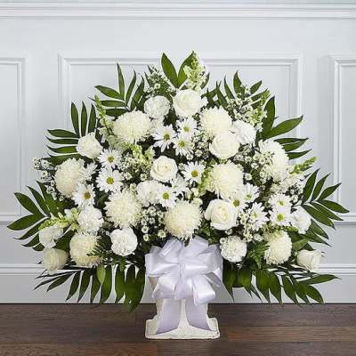 Fan-shaped all-white arrangement with roses, carnations, and daisies in a white container with a bow