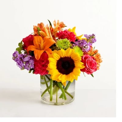 Bright mixed bouquet with sunflower, orange lilies, and pink blooms in a clear glass vase