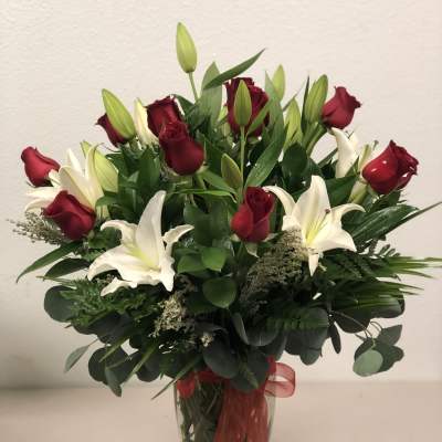Red roses and white lilies in a clear glass vase with a red ribbon