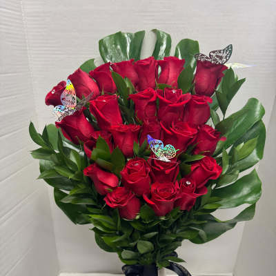 Bouquet of red roses in a tall vase with green leaves and butterfly picks