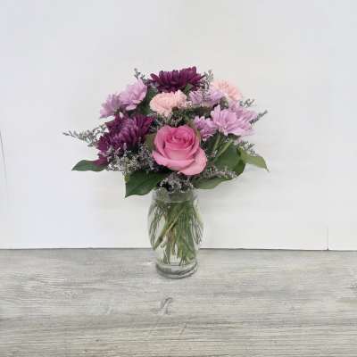 Pink and purple mixed flower arrangement with a rose and mums in a clear glass vase