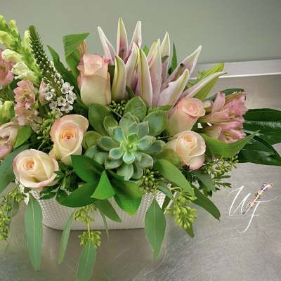 Mixed pink and cream flowers in a white rectangular vase with a succulent center