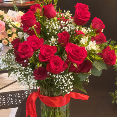 Red roses in a glass vase with white filler flowers and a red ribbon