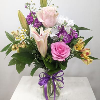 Mixed bouquet of pink roses, lilies, and purple flowers in a glass vase