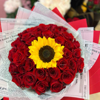 Red rose bouquet with a yellow sunflower center wrapped in newspaper-style paper