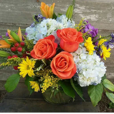 Bouquet of orange roses, blue hydrangeas, and yellow daisies in a vase