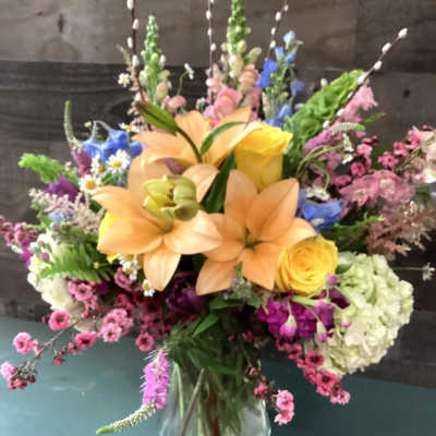 Mixed bouquet with peach lilies, yellow roses, and pink flowers in a glass vase