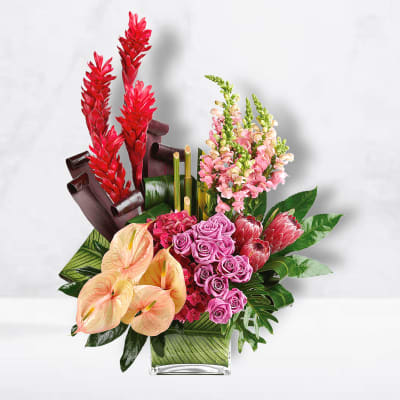 Tropical bouquet with red ginger, pink roses, and peach anthuriums in a glass vase