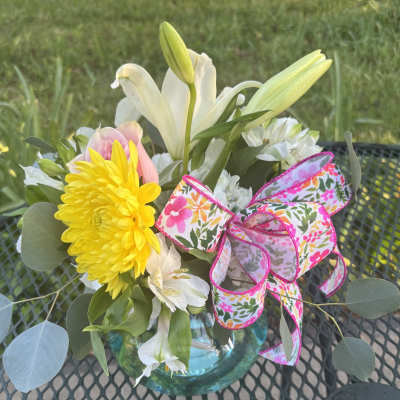 Bouquet of white lilies, yellow chrysanthemum, and pink rose in a glass vase with floral ribbon