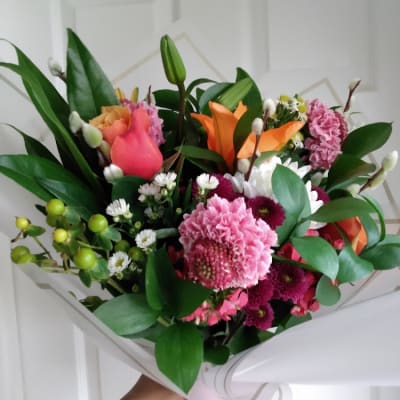 Handheld bouquet of pink, orange, and white flowers wrapped in white paper