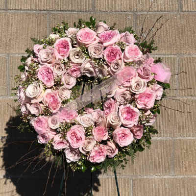 Heart-shaped pink rose wreath with a ribbon on a stand