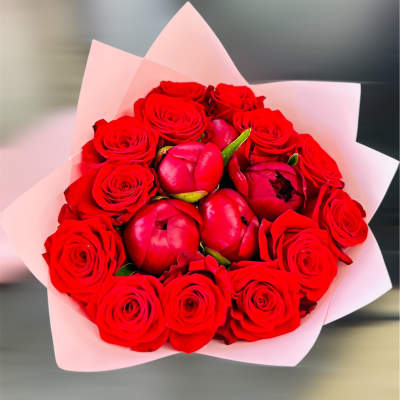Bouquet of red roses and red peonies wrapped in pale pink paper