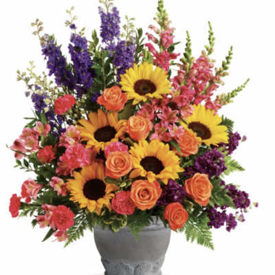 Mixed bouquet with sunflowers, orange roses, and purple spikes in a gray vase