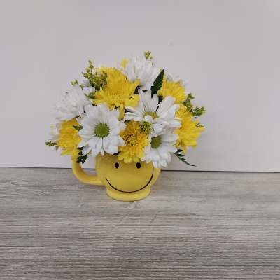 Yellow and white daisy and mum arrangement in a yellow smiley face mug