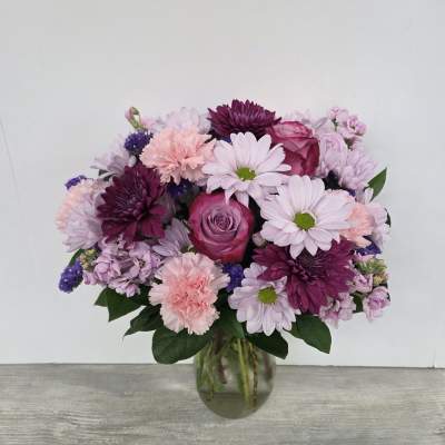 Vase of pink and purple roses, carnations, and daisies arranged in a rounded bouquet