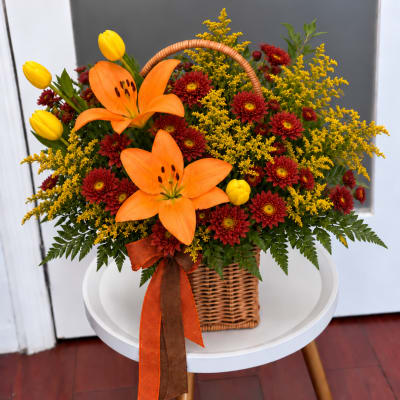 Basket arrangement with orange lilies, yellow tulips, and red mums