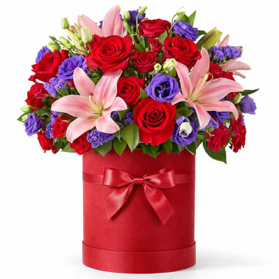 Red roses and pink lilies in a red hatbox with a ribbon