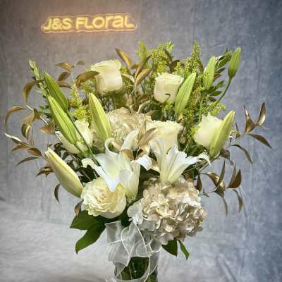 White lilies and roses arranged in a glass vase with a ribbon