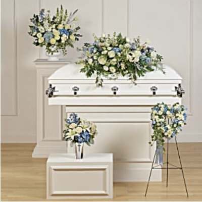 White casket with blue and white floral sprays in a funeral room