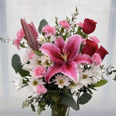 Pink lilies, roses, and daisies arranged in a clear glass vase