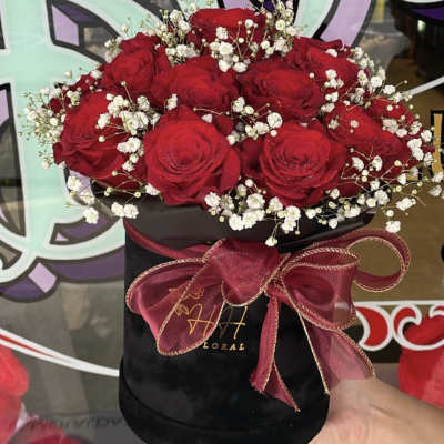 Red roses with white baby's breath in a black hatbox tied with a burgundy ribbon