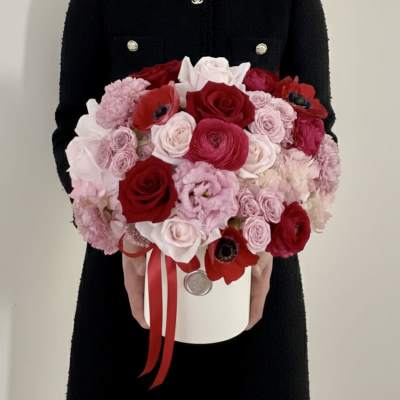 Round bouquet of red, pink, and white flowers in a white hatbox