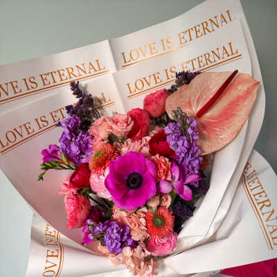 Pink and purple mixed bouquet wrapped in paper with "LOVE IS ETERNAL" text