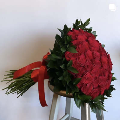 Red rose bouquet with dark greenery and a red ribbon on a stool