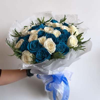 Bouquet of blue and white roses wrapped in white paper with a blue ribbon