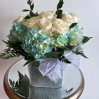 Cream roses and blue hydrangeas in a wrapped bouquet with a white bow