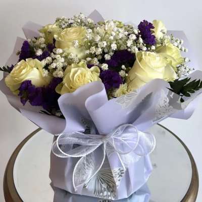 Bouquet of pale yellow roses and purple flowers wrapped in lavender paper