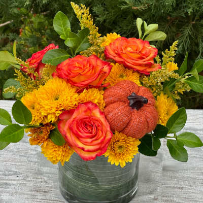 Orange roses and yellow mums in a glass vase with a small pumpkin accent