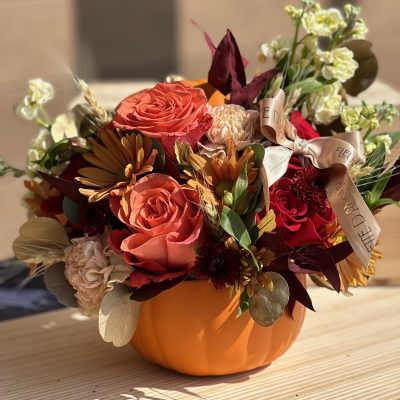 Orange pumpkin-shaped container with mixed autumn flowers and ribbon