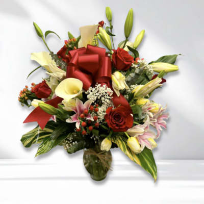 Red roses and cream lilies arranged in a glass vase with a red bow