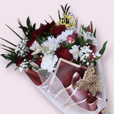Bouquet of red and white flowers wrapped in burgundy paper with a gold topper