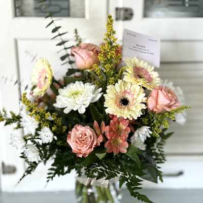 Bouquet of pink roses, white daisies, and yellow filler in a glass vase