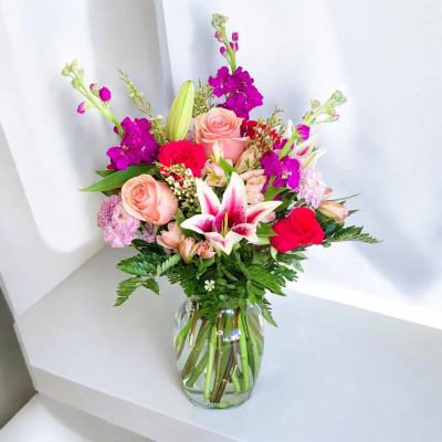 Mixed bouquet of pink roses, lilies, and purple blooms in a glass vase