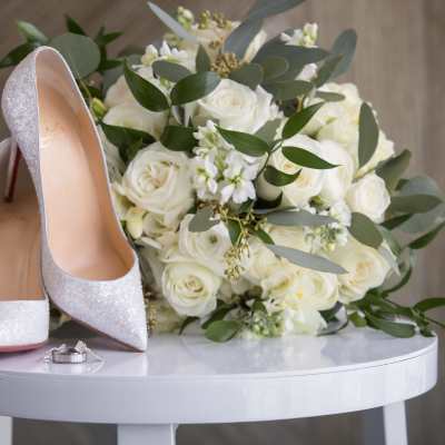 White rose bouquet with silver high heels and wedding rings on a table