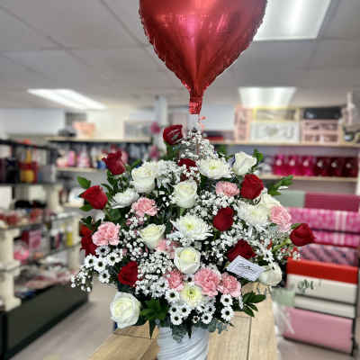 Red heart balloon above a vase of red, white, and pink flowers