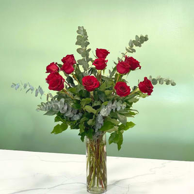 Red roses arranged in a tall glass vase with eucalyptus