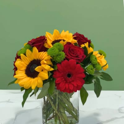 Bouquet of sunflowers, red roses, and a red gerbera daisy in a glass vase