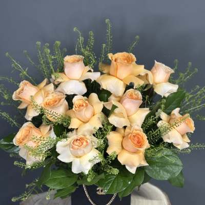 Peach roses arranged in a black box with greenery