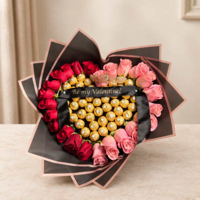 Heart-shaped bouquet of red and pink roses with chocolates and a ribbon