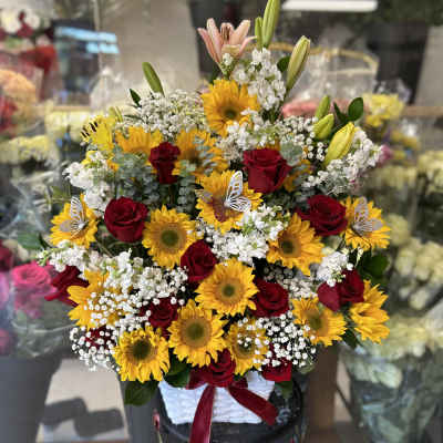 Basket arrangement of red roses, sunflowers, and white filler flowers